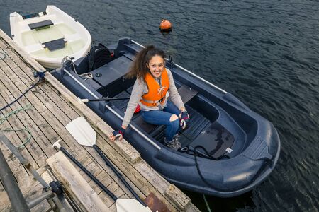 Portrait of young and attractive woman sitting in a boat in orange safe jacket and waiting when they will go somewhere, Norway. Happy face.の写真素材