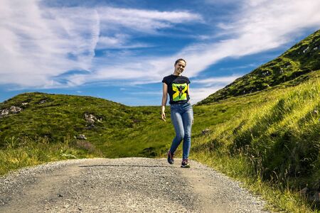 Young woman walking around by countryside road, green field around her, Norway.