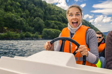 Portrait of young and attractive woman close up driving the motorboat, Norway. She is enjoying the sunny day.の写真素材