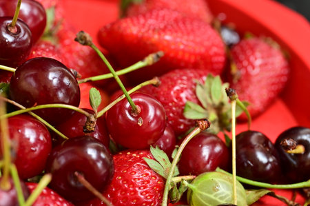 Ripe red cherries and strawberries in a red bowl close upの写真素材