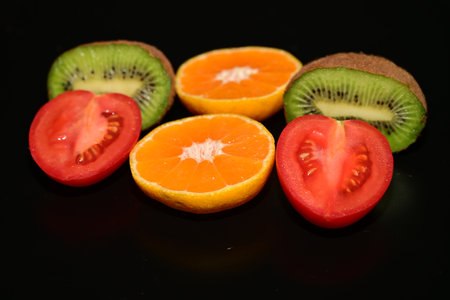 slices of kiwi, orange and tomato on black backgroundの写真素材
