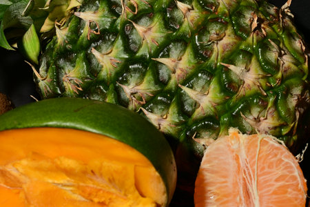 Close up of pineapple and tangerine fruit on black background.