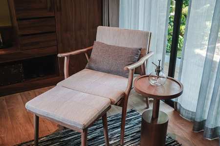 Relaxing wooden chair with cushions in the living room next to the ground floor balcony. Inside the...