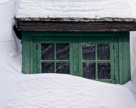 Log cabin buried in deep snow showing only the windowの写真素材