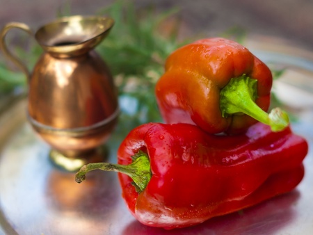 A pair of red capsicum annuum (bell peppers) and a small copper jug.の写真素材