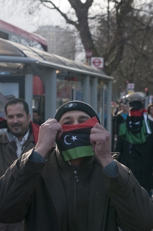 HYDE PARK, LONDON, ENGLAND - March 10, 2011: A demonstrator proudly holds Libyan flag as anti-Gaddafi, pro-democracy protesters rally outside the Libyan Embassy on the corner of Hyde Park, London on March 10, 2011.のeditorial素材