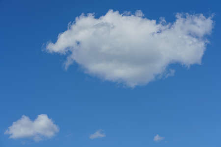 Backdrop from a blue sky with some white fluffy clouds in sunlightの写真素材