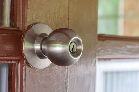 Shiny stainless steel doorknob, attached to the brown wooden doorの写真素材