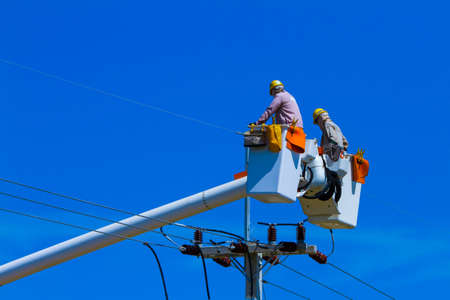 High voltage electricians in the cable car are trying to fix the electrical system with many tools. Which is a high-risk and extremely dangerous job On a clear day.の写真素材