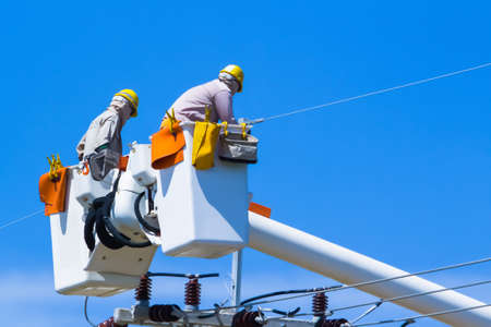 High voltage electricians in the cable car are trying to fix the electrical system with many tools. Which is a high-risk and extremely dangerous job On a clear day.の写真素材