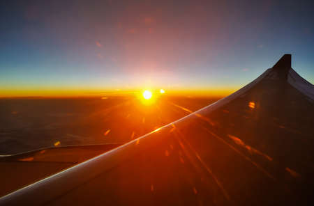 The sunrise at the plane window saw the golden light, clouds and airplane wings. Beautiful twilight light above the sky. Reflected in the plane mirror.の写真素材