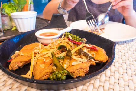 Fried chicken wings on a black plate, served with garnish with freshly ground pepper, dried chilli,...