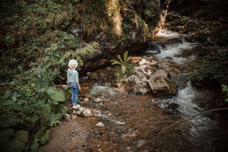 Young tourist woman hiking by mountain river enjoying landscape. Traveler walking along rocks. Summer vacation.の写真素材