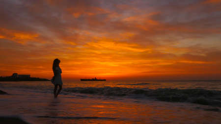 Woman with long hair and summer dress looking at the sea at sunrise. Enjoy the sea breeze in the morning. Colorful summer landscape. A big ship on bacroundの写真素材