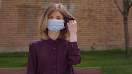Woman takes off medical mask. Close up portrait young Caucasian smiling looking at camera. Outdoor health care concept. End pandemic coronavirus COVID-19. No more surgical maskの写真素材