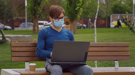 Young caucasian man in casual-wear sitting cross-legged on ground and working on laptop. Freelancer working outside typing on laptop computer. Red wall on the background.の写真素材