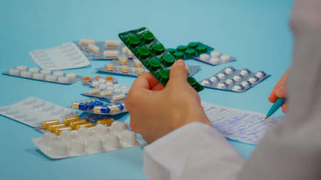 Doctor hand writing a prescription holding a pill blister. Pile of pills in blister packs on blue background.の写真素材