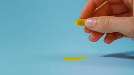 Woman hand holding an open medicine capsule with a yellow powder inside. Medicine pills on blue backround. Pharmaceutical Concept. Pills treatment.の写真素材