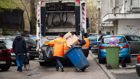 BUCHAREST, ROMANIA - May 15, 2021: White Garbage truck used for Collection of waste or garbage in Bucuresti. Two workers loading mixed domestic waste in waste collection truckのeditorial素材