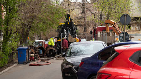 BUCHAREST, ROMANIA - May 15, 2021: Workers carry out repair work on the city sewer. Tractor, hole in the asphalt.のeditorial素材