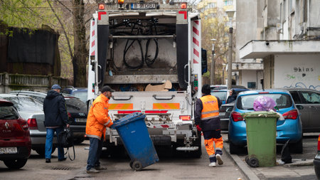 BUCHAREST, ROMANIA - May 15, 2021: White Garbage truck used for Collection of waste or garbage in Bucuresti. Two workers loading mixed domestic waste in waste collection truck from townのeditorial素材