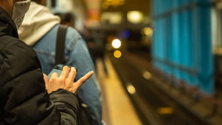 Woman in a protective mask, standing on the platform of a subway station during a pandemic ..with a mobile phone in her hands while waiting for a trainのeditorial素材