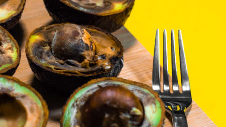 Contaminated tropical fruits. Bad Avocado Half Close up on Yellow background. Bad Vegan food. Rotten Avocado on wood Chipper. Copy space Necomestibile Food. Stop wasting food. Overripe Fruits Concept.の写真素材