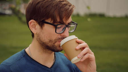 Young sad man. Unhappy alone man working outdoor. Closeup face of handsome guy with sad eyes, on the nature drink coffee.の写真素材