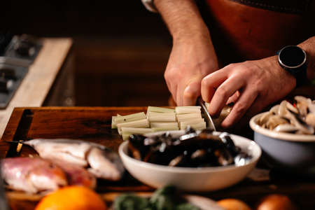 Cook chopping celery on cutting board surrounded by a variety of ingredients. Fresh Mollusks Fish Shell Shrimp. Cooking Seafood.の写真素材