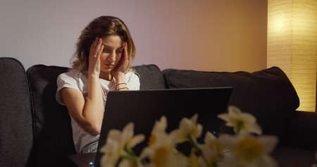 Woman working on laptop alone in dark living late at nightの写真素材