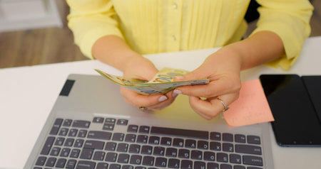 Woman counting money over a laptop keyboard. Handheld money being numbered by an accountant.の写真素材