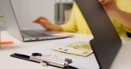 Woman hands typing on keyboard then opening the clipboard and raising a pile of money.