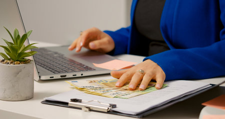 Woman in office opening a folder and flipping the bills apart to count. Money investing in assets by...