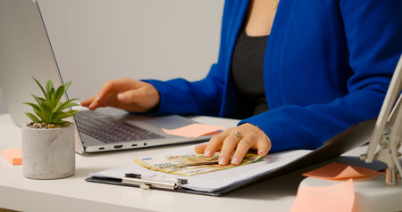 Woman in office opening a folder and flipping the euro bills apart to count. Female boss counting...