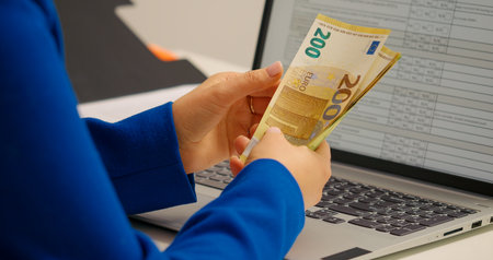 Side view woman that counts money in bills in front of a laptop. Female cashier counting cash money.の写真素材