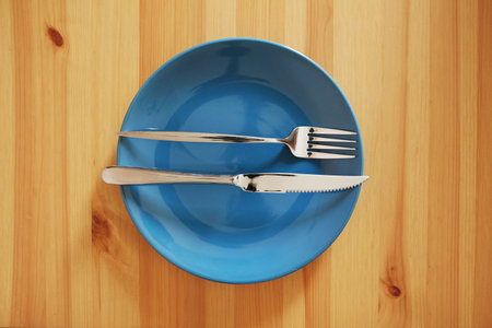 A signal "The dish is wonderful". Empty and clean blue plate with fork and knife on a wooden table as an example of table etiquetteの写真素材