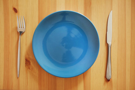 Empty and clean blue plate with fork and knife on a wooden table as an example of table etiquetteの写真素材