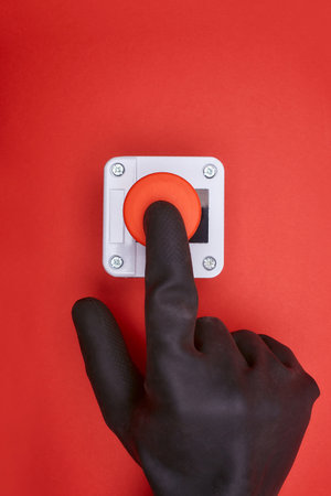The hand in black vinyl glove, which pushes the emergency button at the red background at the top viewの写真素材