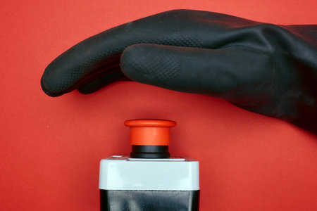 The hand in black resin glove, which is ready to push the emergency button at the red background at the side viewの写真素材