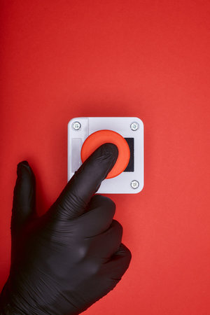 The hand in black vinyl glove, which pushes the emergency button at the red background at the top viewの写真素材