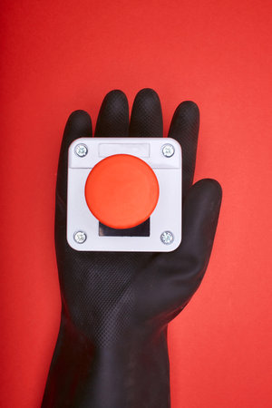 The hand in black resin glove, which keep the emergency button at the red background at the top viewの写真素材