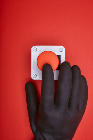 The hand in black resin glove, which pushes the emergency button at the red background at the top viewの写真素材