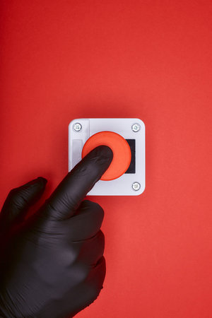 The hand in black vinyl glove, which pushes the emergency button at the red background at the top viewの写真素材