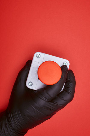 The hand in black resin glove, which constrict the emergency button at the red background at the top viewの写真素材