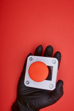 The hand in black vinyl glove, which keep the emergency button at the red background at the top viewの写真素材