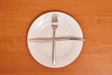 A signal "I'm waiting for the next meal". Empty and clean blue plate with fork and knife on a wooden table as an example of table etiquetteの写真素材
