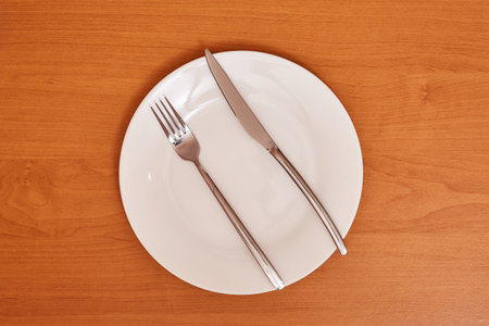 A signal "The meal was hearty and there was plenty of it". Empty and clean blue plate with fork and knife on a wooden table as an example of table etiquetteの写真素材