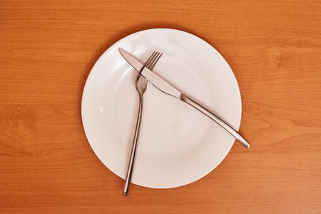 A signal "Didn't like the dish". Empty and clean white plate with fork and knife on a wooden table as an example of table etiquetteの写真素材