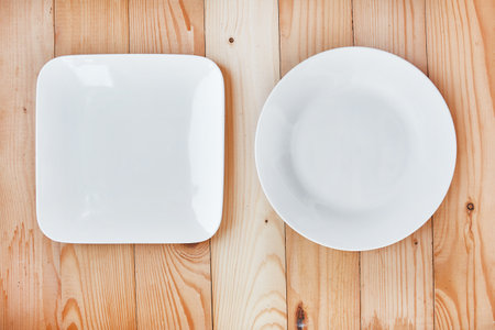 Round and square empty clean plates on wooden background at top viewの写真素材