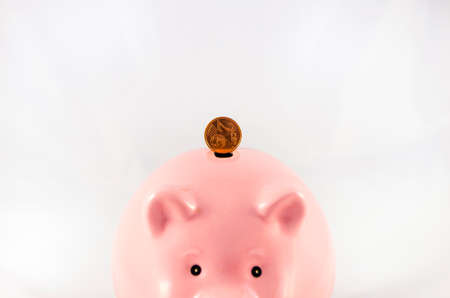 Golden coins falling into a piggy bank isolated on white の写真素材